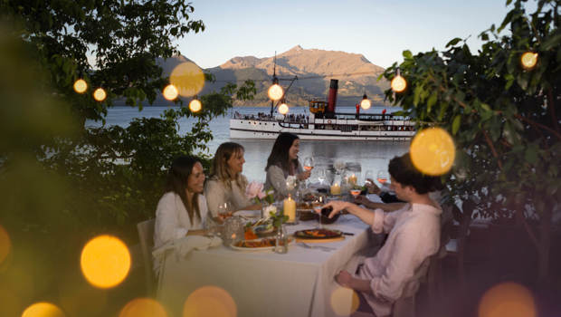 A group of friends enjoy a sunset dinner experience at Walter Peak with the Earnslaw in the background.