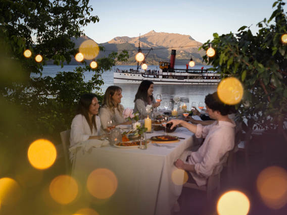 A group of friends enjoy a sunset dinner experience at Walter Peak with the Earnslaw in the background.