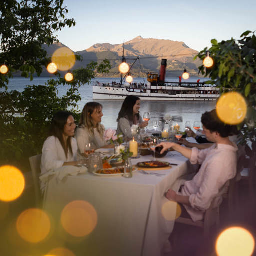 A group of friends enjoy a sunset dinner experience at Walter Peak with the Earnslaw in the background.