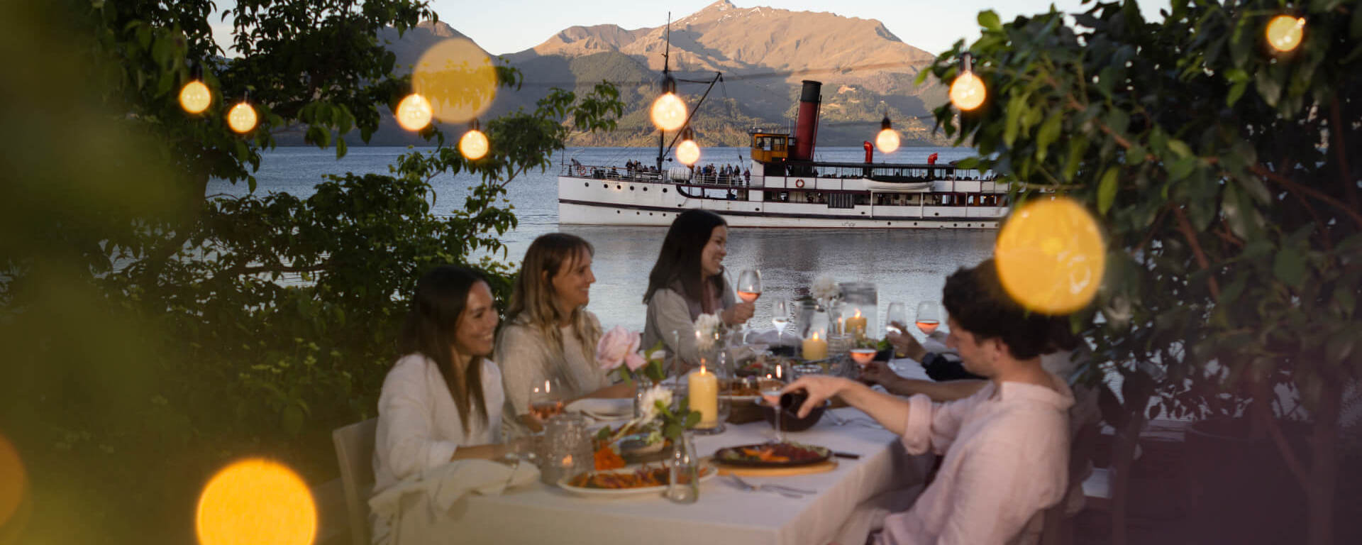 A group of friends enjoy a sunset dinner experience at Walter Peak with the Earnslaw in the background.