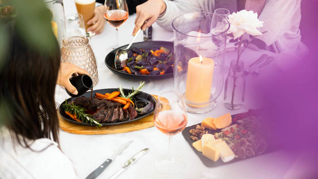 A gravy is poured over freshly carved meat with salads and a cheese board in the background.