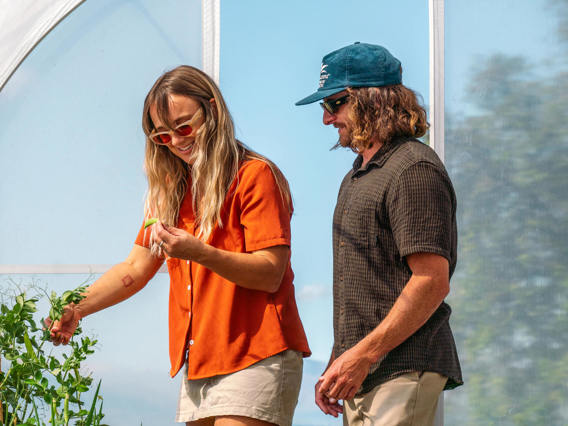 A couple explores Walter Peak’s Eco Experience greenhouse, harvesting fresh vegetables and enjoying a hands-on sustainable experience.