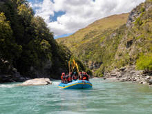 Rafters celebrating with paddles raised high while drifting through a serene canyon on the turquoise waters of the Shotover River.