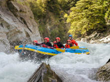 Thrilled rafters splashing through fast-moving rapids surrounded by dramatic cliffs and lush greenery on the Shotover River.