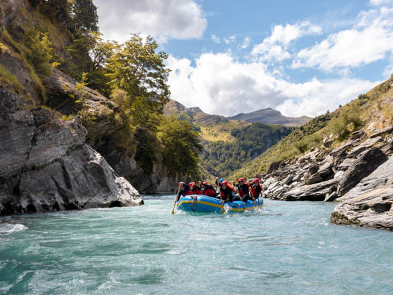 Rafting group paddling through turquoise waters in a scenic canyon surrounded by rocky cliffs and lush greenery on the Shotover River.