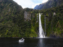 Wide shot of The Sovereign vessel cruising in front of a waterfall on Milford Sound