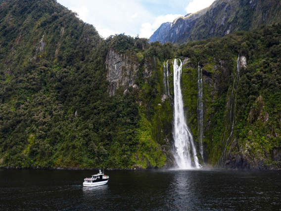 Wide shot of The Sovereign vessel cruising in front of a waterfall on Milford Sound