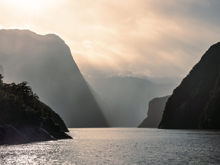 A moody photo of Milford Sound on a rainy day with layers of the towering cliffs showing.