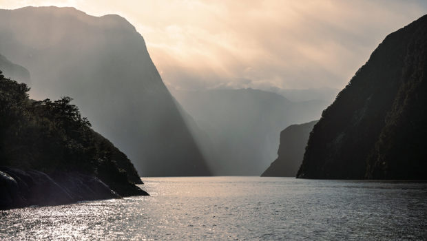 A moody photo of Milford Sound on a rainy day with layers of the towering cliffs showing.