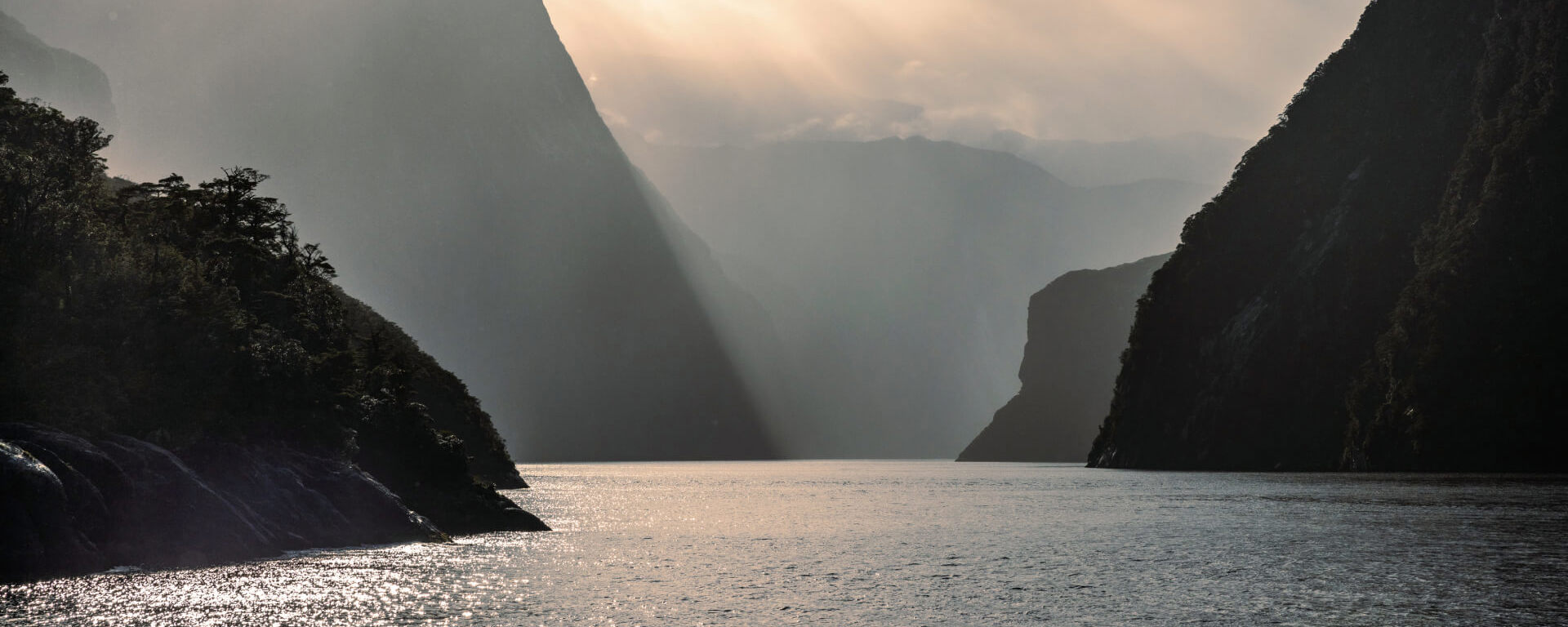 A moody photo of Milford Sound on a rainy day with layers of the towering cliffs showing.