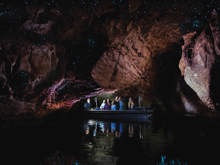 A small boat glides through the Te Anau glowworm caves, where visitors gaze at thousands of glowing blue lights on the cave ceiling, reflecting off calm waters.