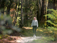 A woman walks along a forest path surrounded by lush greenery and dappled sunlight, enjoying the serene natural beauty near the Te Anau Glowworm Caves.