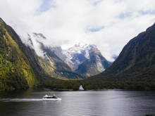 Wide shot of a vessel cruising in Milford Sound with snow covered mountains in the background