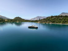 Spirit of Queenstown cruise boat on the tranquil waters of Bob’s Cove, surrounded by lush greenery and mountain landscapes under a clear blue sky.