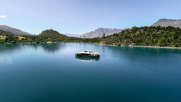 Spirit of Queenstown cruise boat on the tranquil waters of Bob’s Cove, surrounded by lush greenery and mountain landscapes under a clear blue sky.