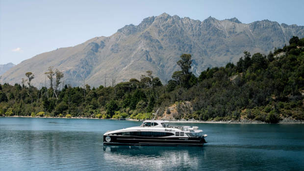 Spirit of Queenstown cruise boat gliding on Lake Wakatipu with rugged mountain peaks and lush greenery in the background on a sunny day.