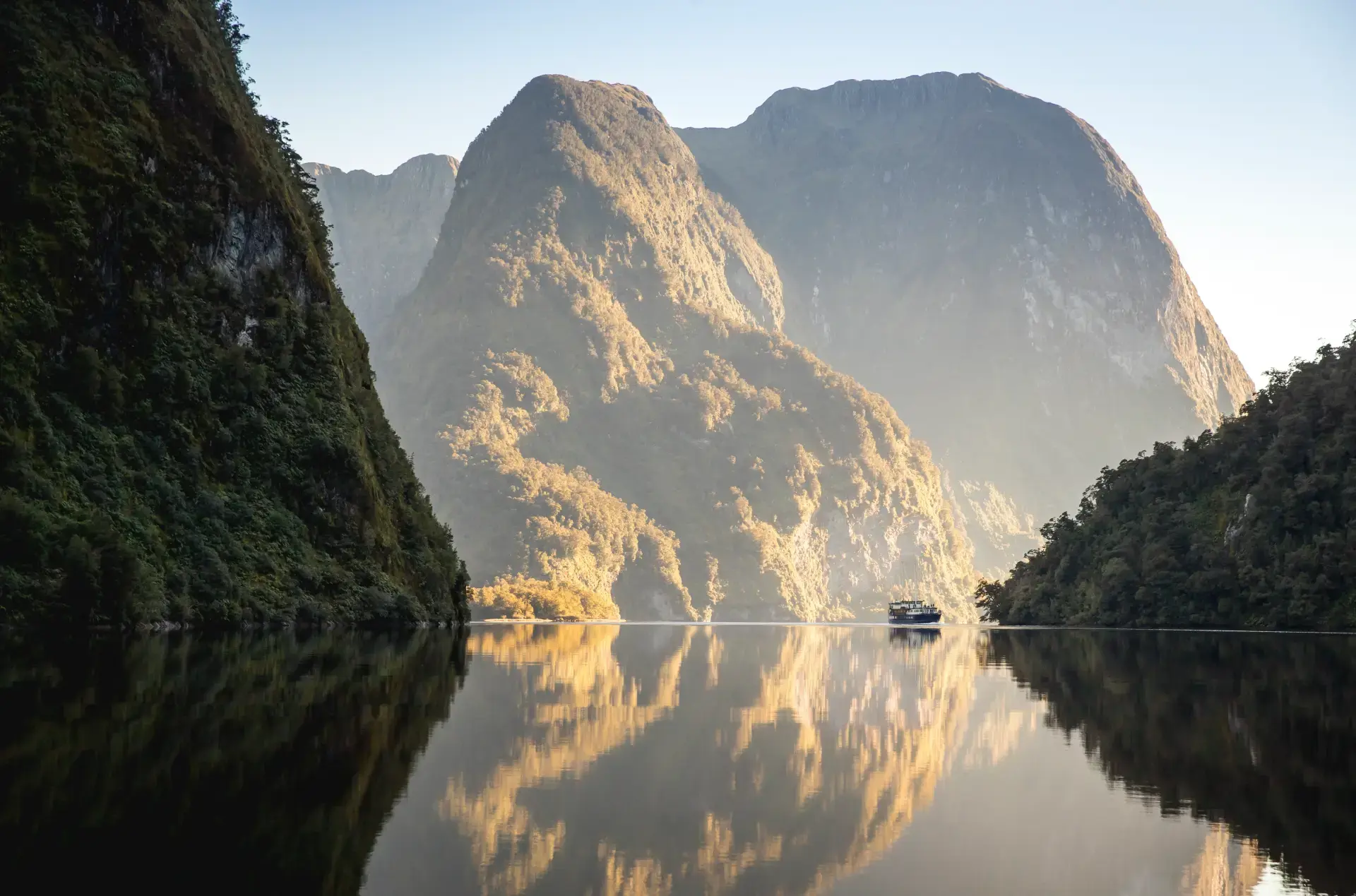 The Fiordland Navigator boat anchors in a quite arm of Doubtful Sound amongst still waters with a clear reflection of the surrounding towering mountains.